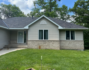 Victoria roofing contractor project - single-story house with grey roof, beige siding, brick facade, and green lawn.