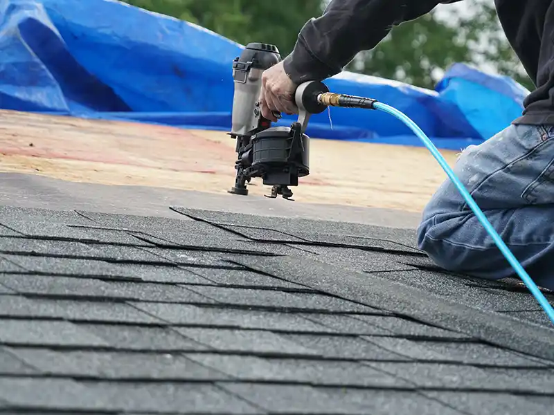 Close up of a roofer installing new gray shingles on a roof with a nail gun